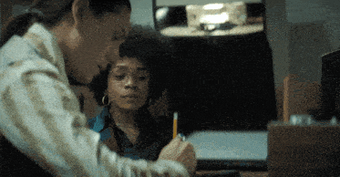 two women are sitting at a desk with a pencil in their hand