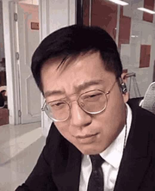 a man in a suit and tie is wearing glasses and headphones while sitting at a desk .