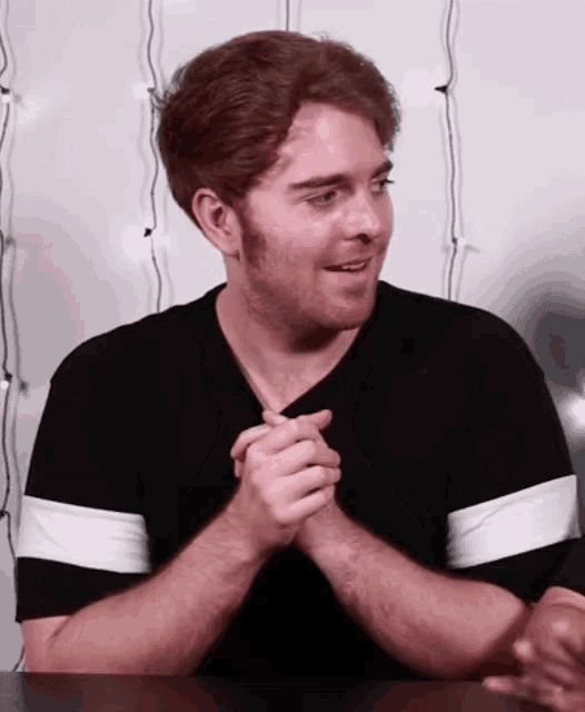 a man with red hair is sitting at a table with his hands folded in prayer .