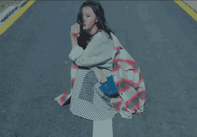 a woman wearing a plaid coat sits on the side of the road