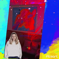 a woman is standing in front of a painting in a room with the word picsart on the bottom