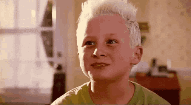 a young boy with white hair is wearing a green shirt and looking up .