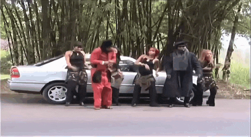 a group of people are standing next to a silver car