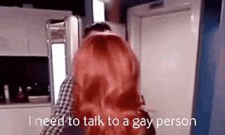 a woman with red hair is standing next to a man in a kitchen and talking to a gay person .