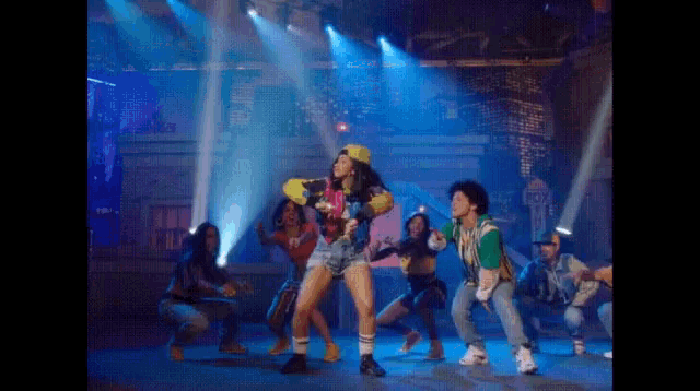 a group of people are dancing on a stage with blue lights behind them