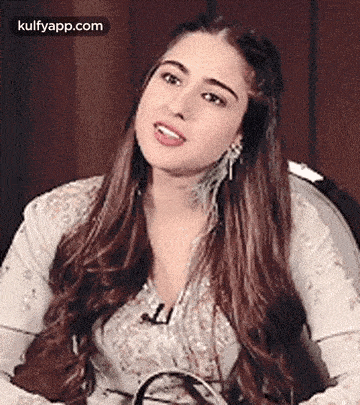 a woman with long brown hair is sitting in a chair and looking at the camera .