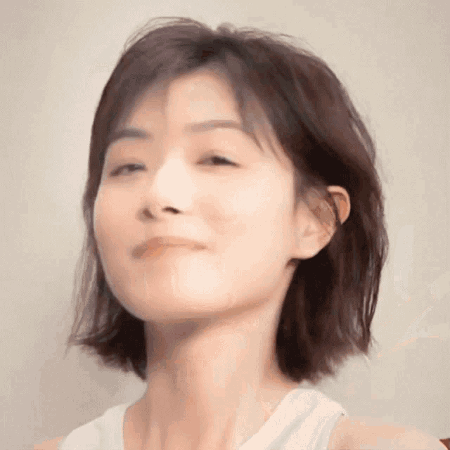 a close up of a woman 's face with a white tank top on .