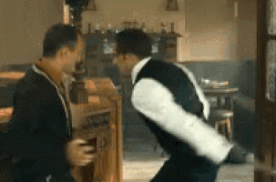 two men are dancing in a room and one is holding a glass