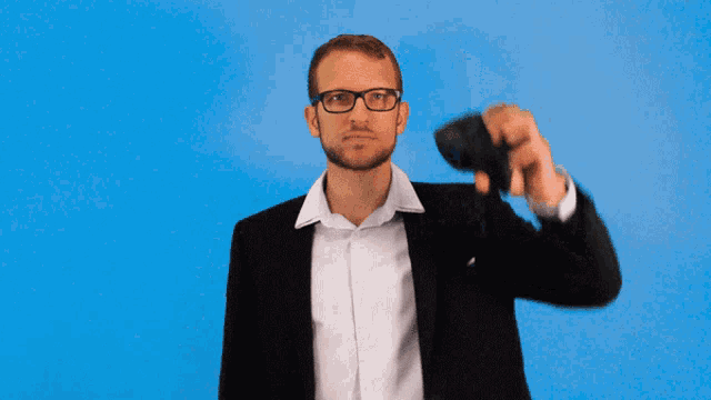 a man in a suit and glasses is holding a remote control