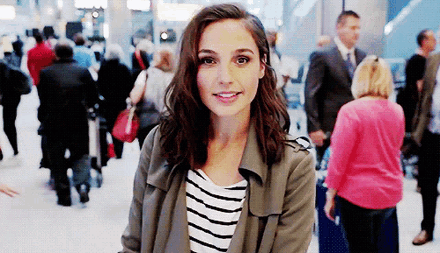 a woman wearing a striped shirt and a trench coat smiles in front of a crowd