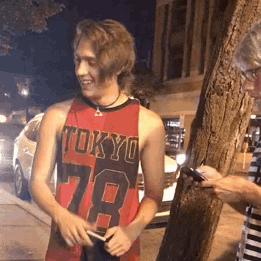 a man wearing a tokyo 78 jersey is standing next to a tree at night