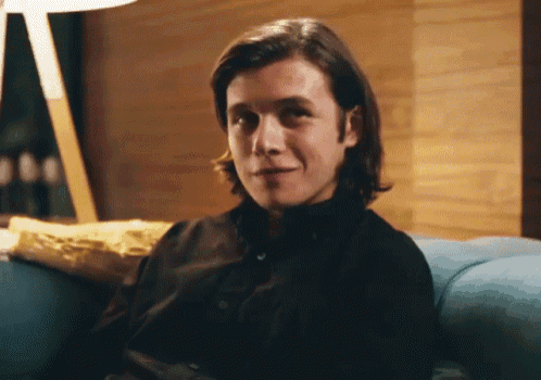 a man with long hair is sitting on a blue couch and smiling