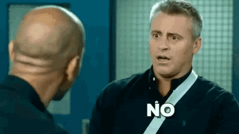 a bald man is talking to another bald man in a room and the man is saying `` no '' .