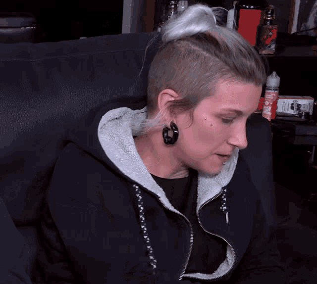 a woman sitting on a couch with a bun on her head and a bottle of e liquid in the background