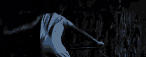 a person in a blue shirt is standing in a dark room holding a stick .