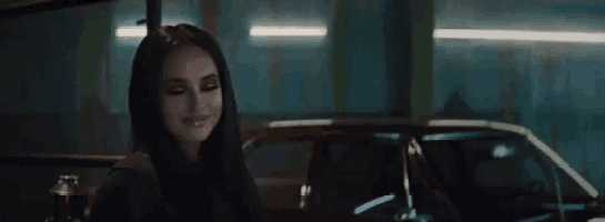 a woman is smiling while standing next to a red car in a parking garage .