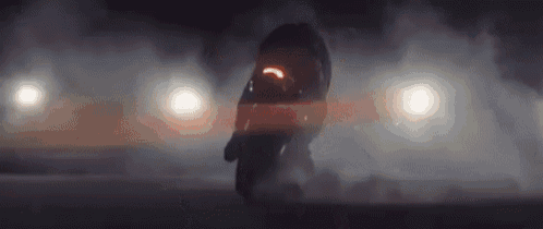 a car is doing a trick on a track at night with smoke coming out of it .