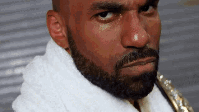a man with a beard and a white towel around his neck looks at the camera