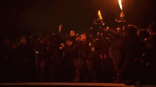 a group of people standing on a stage with a large fire coming out of the middle