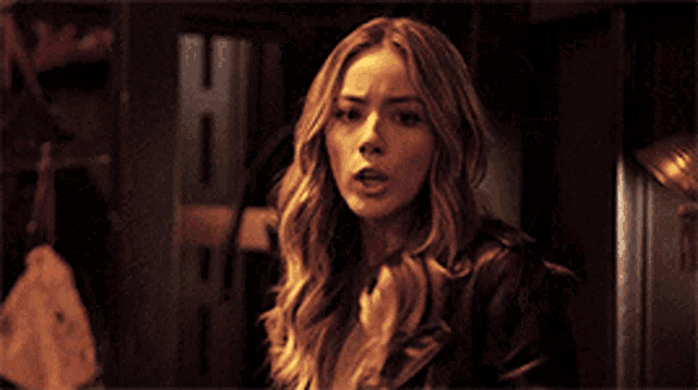 a woman with long blonde hair is standing in a dark room and looking at the camera