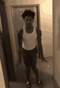 a man in a white tank top and shorts is standing in a hallway next to a door .
