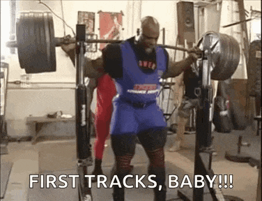 a man is squatting with a barbell in a gym and says `` first tracks , baby !! ''