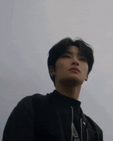 a young man wearing a black jacket and a black turtleneck is looking up at the sky .