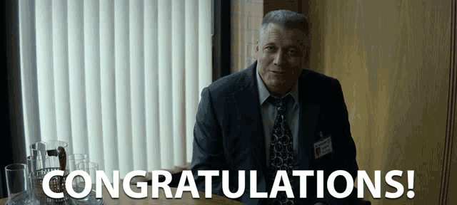a man in a suit and tie is sitting at a table with the words congratulations written in front of him