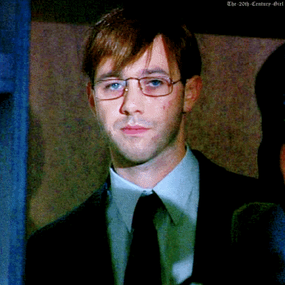 a man wearing glasses and a suit looks at the camera