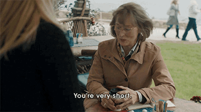 a woman sitting at a table talking to another woman and says " you 're very short "