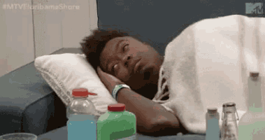 a man is laying on a bed with his head on a pillow next to bottles of water .