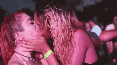 two women are kissing in front of a crowd of people at a concert .