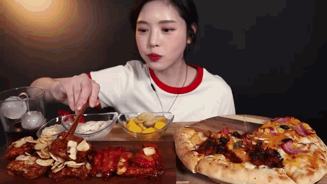 a woman is sitting at a table eating pizza and chicken with chopsticks .