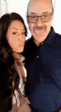 a man with glasses and a mustache is standing next to a woman with her tongue out .