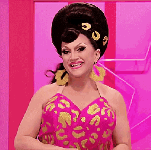 a woman in a pink and gold dress is smiling and wearing a large wig .