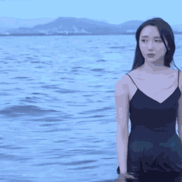 a woman in a black dress is standing on a beach with her eyes closed