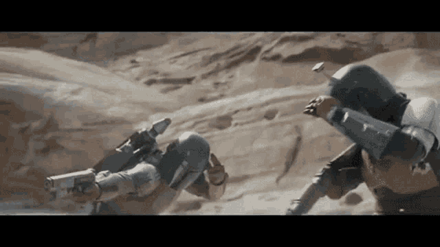 two soldiers are fighting in the desert and one of them is holding a gun .