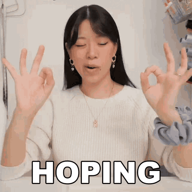 a woman in a white sweater is making an ok sign and the word hoping is behind her