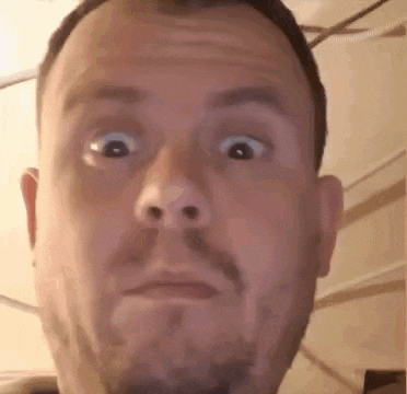 a man with a beard is making a funny face with his eyes wide open .
