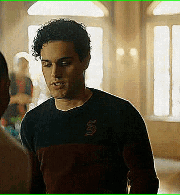 a man with curly hair wearing a black and red sweater with the letter s on it