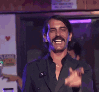 a man with a mustache is giving a thumbs up sign while wearing a suit .
