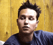 a man with a mohawk is sitting in front of a wooden wall and making a funny face .