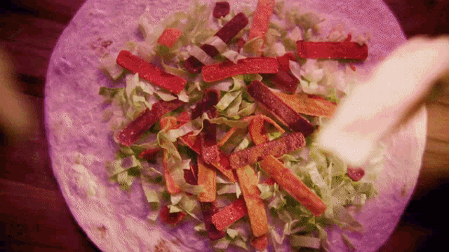 a purple tortilla with lettuce carrots and peppers on it