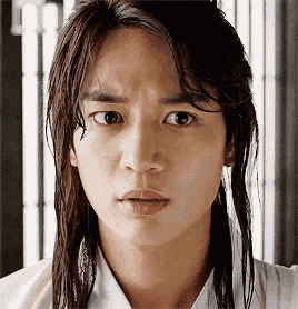 a close up of a young man 's face with long hair making a funny face .