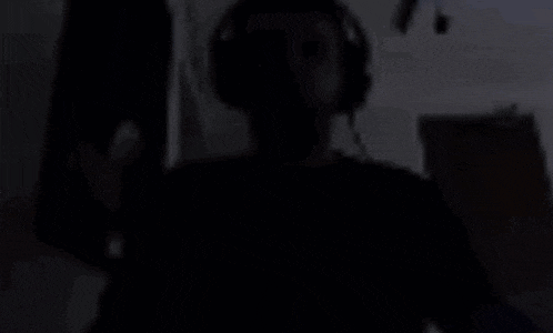 a man wearing headphones and a black shirt is standing in a dark room .