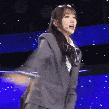 a girl in a suit and tie is dancing on a stage with her arms outstretched .