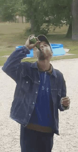 a man wearing a blue shirt with the letter b on it drinks from a can