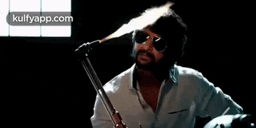 a man wearing sunglasses and a white shirt is holding a microphone in his hand .