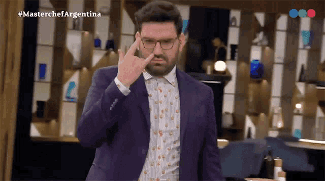 a man in a suit and glasses is giving the middle finger in front of a screen that says masterchef argentina
