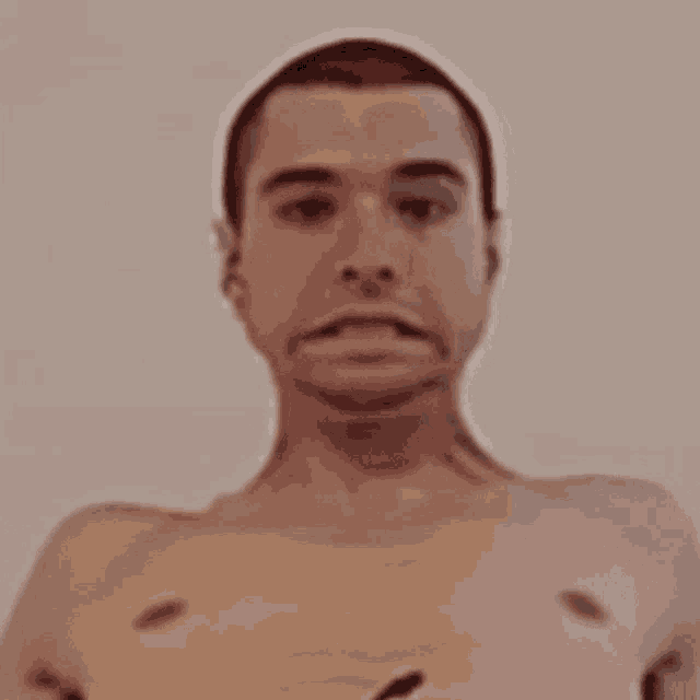 a shirtless man with a tattoo on his chest is making a face .